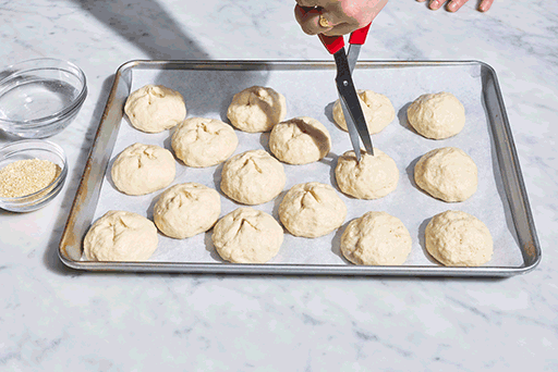 Using kitchen shears to snip the tops of gluten-free rolls before baking.