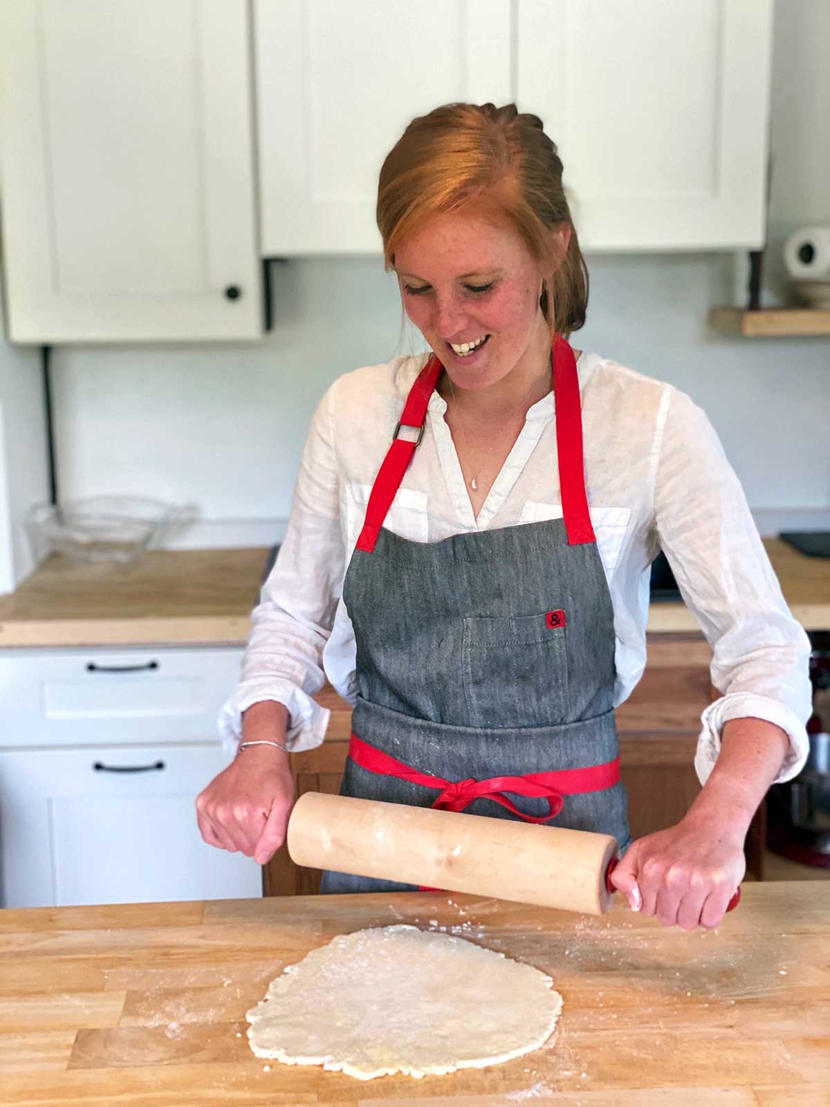 A woman with an apron on rolling out pie dough with a rolling pin