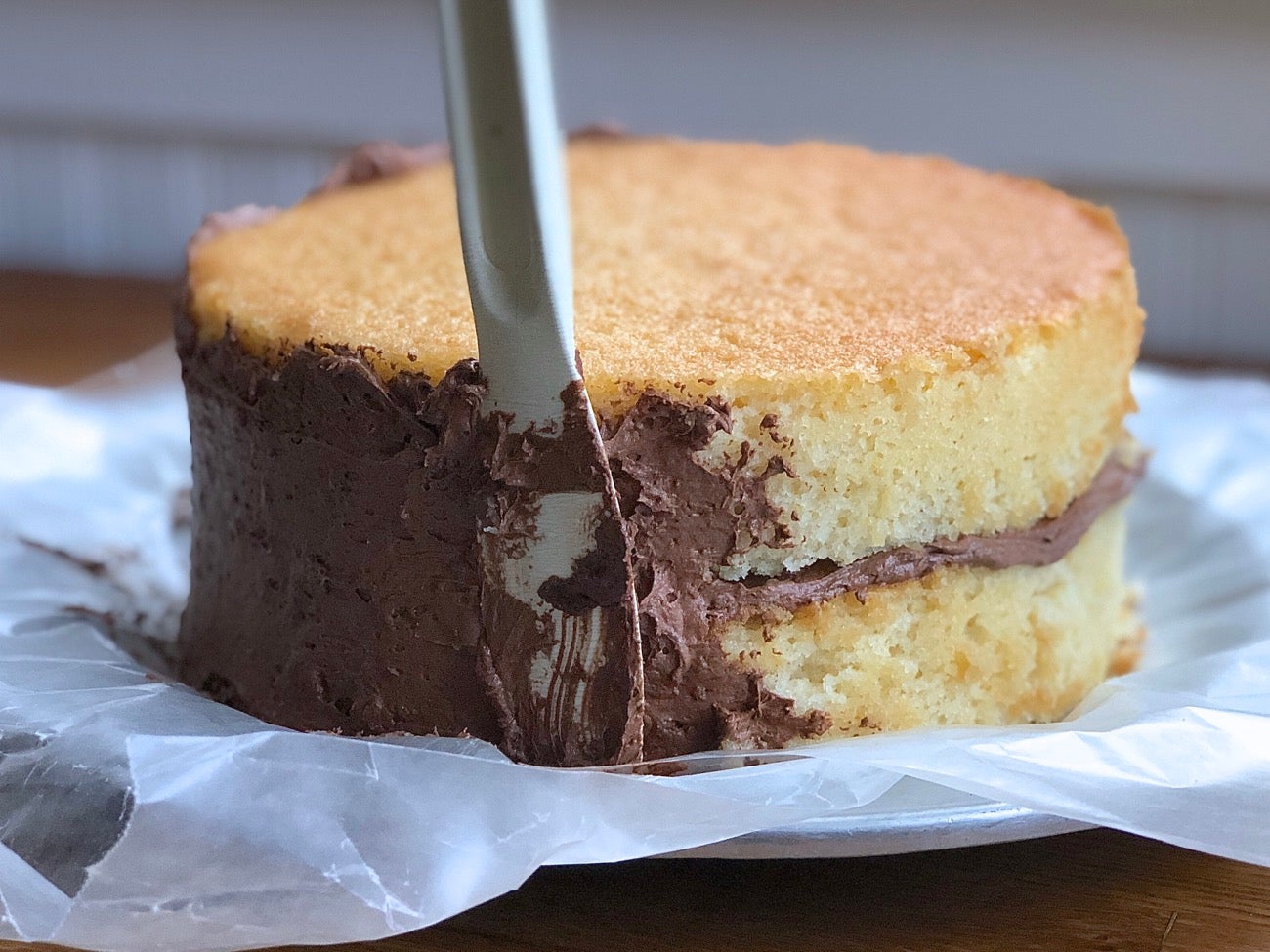 Applying a layer of chocolate frosting — the crumb coat to a double layer yellow cake.