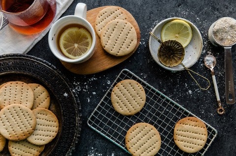 A batch of Digestive Tea Biscuits on a cooling rack with a couple cups of tea