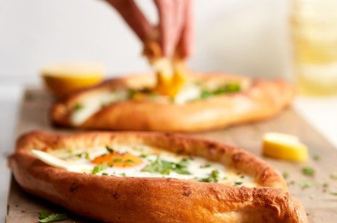A hand dipping a piece of bread into the soft yolk of khachapuri (Georgian Cheese Bread) - select to zoom
