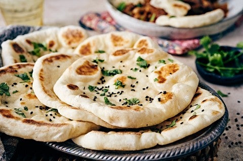Several pieces of freshly cooked naan on a plate, garnished with herbs and ghee - select to zoom