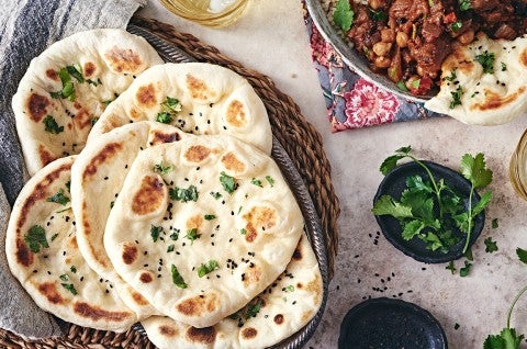 Freshly baked Naan bread in a basket next to a bowl of herbs and chutney - select to zoom