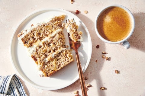 An overhead photo of a slice of Hummingbird Cake on a plate with a fork resting on the edge. You can see the tender cake layers with cream cheese pineapple frosting sandwiched between them.  - select to zoom