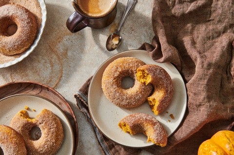 A few baked pumpkin donuts dusted in cinnamon sugar on plates, ready to be eaten. - select to zoom