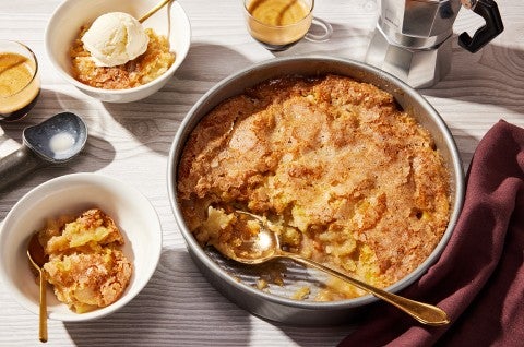 A round pan of Sugar-Crusted Apple Cobbler with a spoonful portioned into a small bowl. - select to zoom