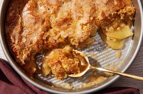 A close-up shot a round pan of Sugar-Crusted Apple Cobbler with a spoonful portioned - select to zoom