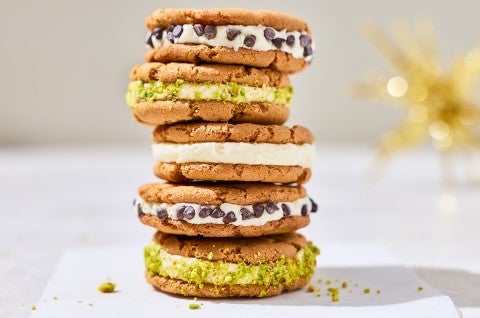Stacked cannoli sandwich cookies showing the cookies, a layer of filling, and chocolate chips or pistachio coating.