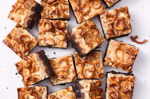 Showing a dozen gluten free chocolate seven layer bars from above with golden hues of caramel and nuts from above. - select to zoom
