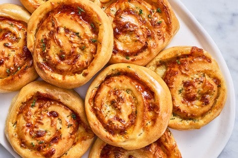 Overhead photograph of gluten free garlic parmesan swirl buns stacked on a light plate showing golden baked buns.