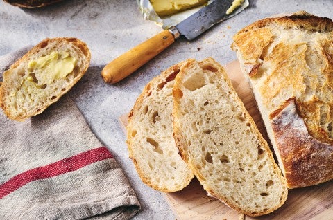 Fresh baked loaf of No-Knead Crusty White Bread on a table with jam and butter and slices on a cutting board. - select to zoom