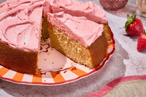 Brown Sugar Strawberry Frosted Cake seen from the side showing a thick layer of frosting and a golden cakey interior. - select to zoom