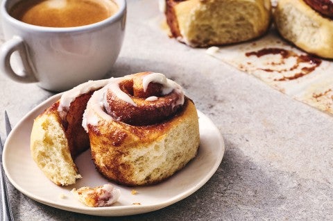 A Sourdough Cinnamon Roll on a plate accompanied by coffee - seen from the side. - select to zoom