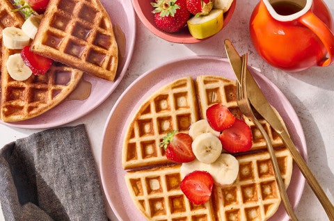 A Belgian Style Yeast Waffle on a plate with fresh strawberries and banana. - select to zoom