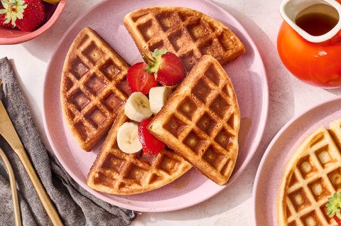 A Belgian Style Yeast Waffle on a plate with fresh strawberries and banana. - select to zoom
