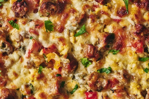 Detailed shot of breakfast pizza showing veggies, melted cheese, eggs, sausage, and herbs - select to zoom