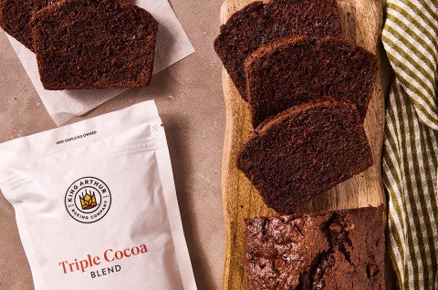 Double Chocolate Zucchini Bread on a cutting board with a bag of triple cocoa blend by King Arthur Baking - select to zoom