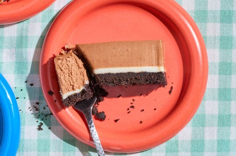 A bite of a No-Bake Chocolate Cheesecake Bar on a fork seen from overhead with a red plate and a teal checkered tablecloth - select to zoom