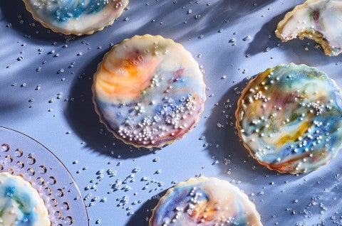 Northern Lights Iced Sugar Cookies arranged on a blue background surrounded by sprinkles of sparkling sugar - select to zoom