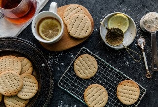 A batch of Digestive Tea Biscuits on a cooling rack with a couple cups of tea