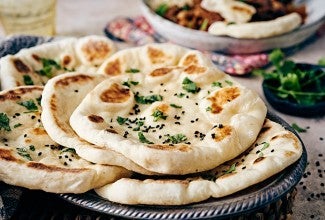 Several pieces of freshly cooked naan on a plate, garnished with herbs and ghee