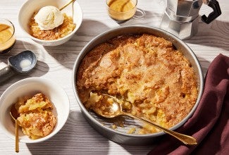 A round pan of Sugar-Crusted Apple Cobbler with a spoonful portioned into a small bowl.