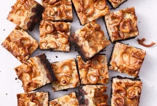 Showing a dozen gluten free chocolate seven layer bars from above with golden hues of caramel and nuts from above.