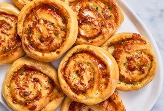 Overhead photograph of gluten free garlic parmesan swirl buns stacked on a light plate showing golden baked buns.