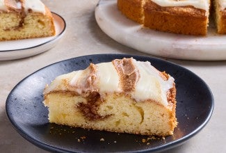 Cinnamon Roll Cake on a dark plate shown from the side with a strong layer of cinnamon and sugar inside the golden cake.