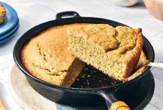 A slice of Sourdough Cornbread being removed from a cast iron skillet.