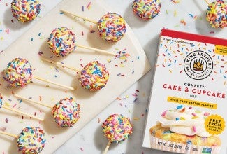 Confetti Cake Pops on a countertop with a box of confetti cake and cupcake mix made by King Arthur Baking in the frame. Seen from above.