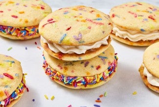 Confetti Whoopie Pies stacked on a counter with sprinkles decorating the filling around the outside of the whoopie pies.