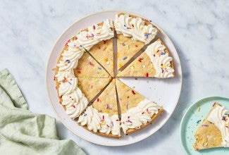 Sliced Confetti Sugar Cookie Cake on a marble countertop with a piece on a plate.