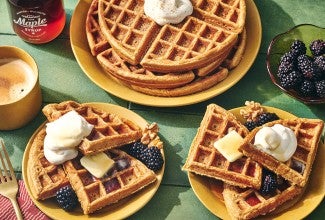 Gingerbread Waffles on a green countertop with some on plates and others stacked.