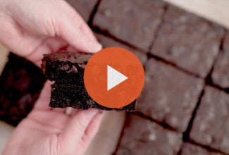 Breaking apart a fudge brownie with an orange play icon over the image. - select to zoom
