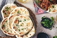 Freshly baked Naan bread in a basket next to a bowl of herbs and chutney