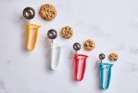 Different sizes of kitchen scoops next to chocolate chip cookies