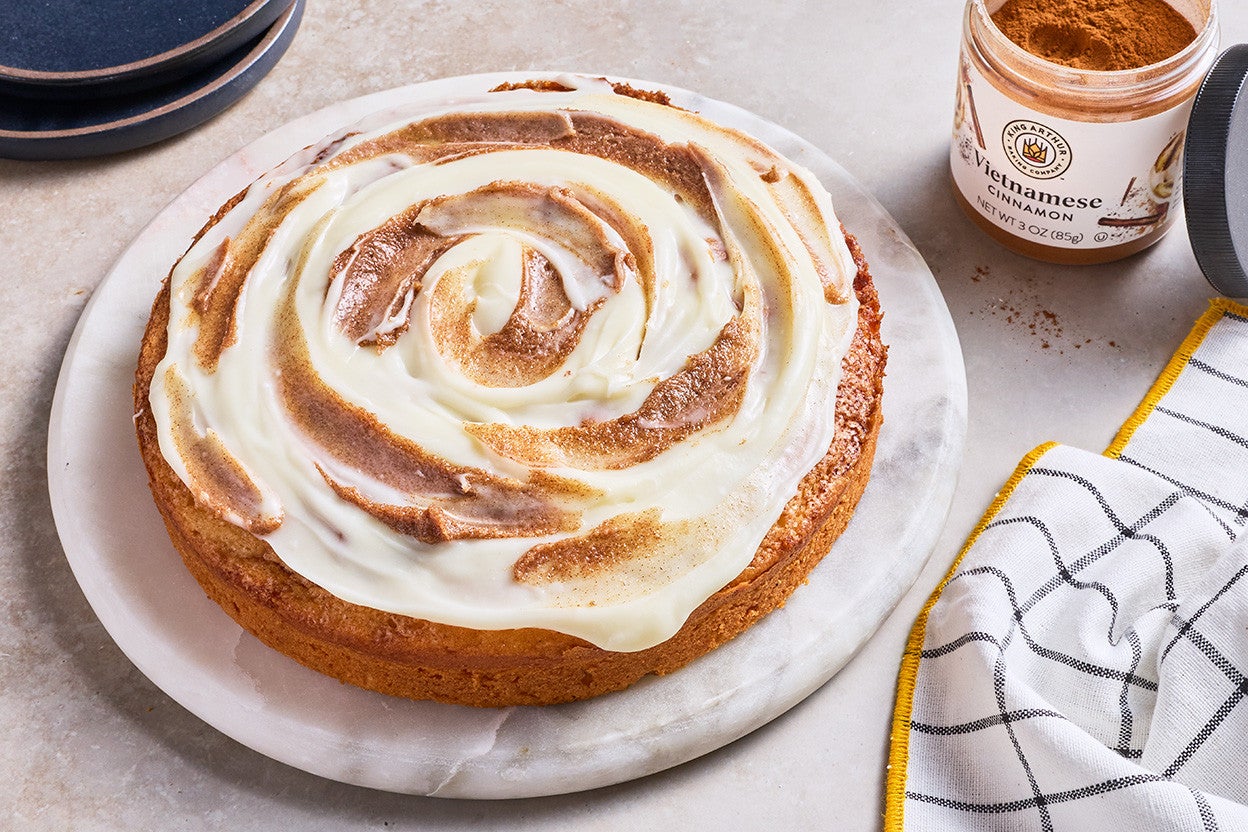 Cinnamon Roll Cake on a marble round cake platter and a jar of Vietnamese cinnamon in the background.