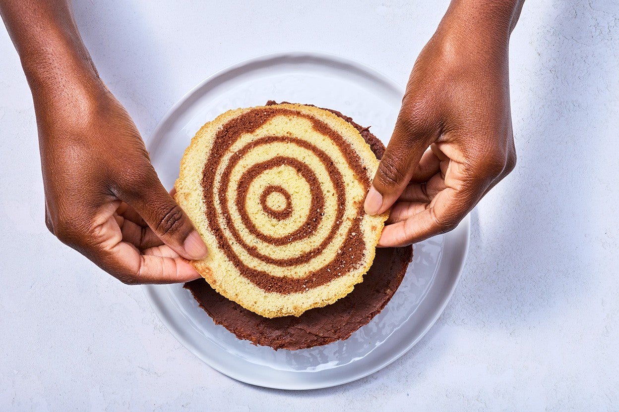 Placing a sliced top of Souche de Noël on a freshly baked cake showing rings of clearly baked vanilla and chocolate cake.