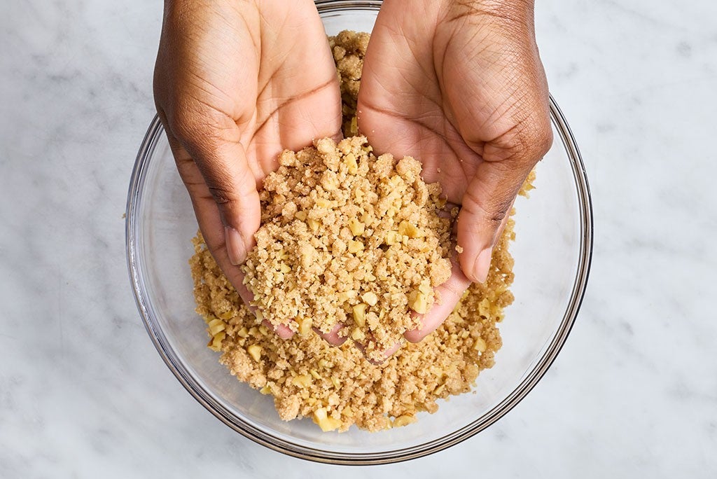 Two hands seen from above mixing crumble in a glass bowl