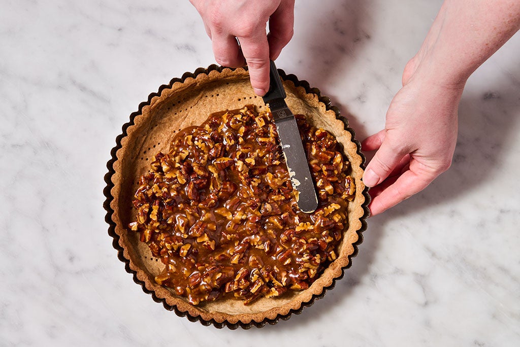 A person spreading caramel mixture into a tart crust using an offset spatula