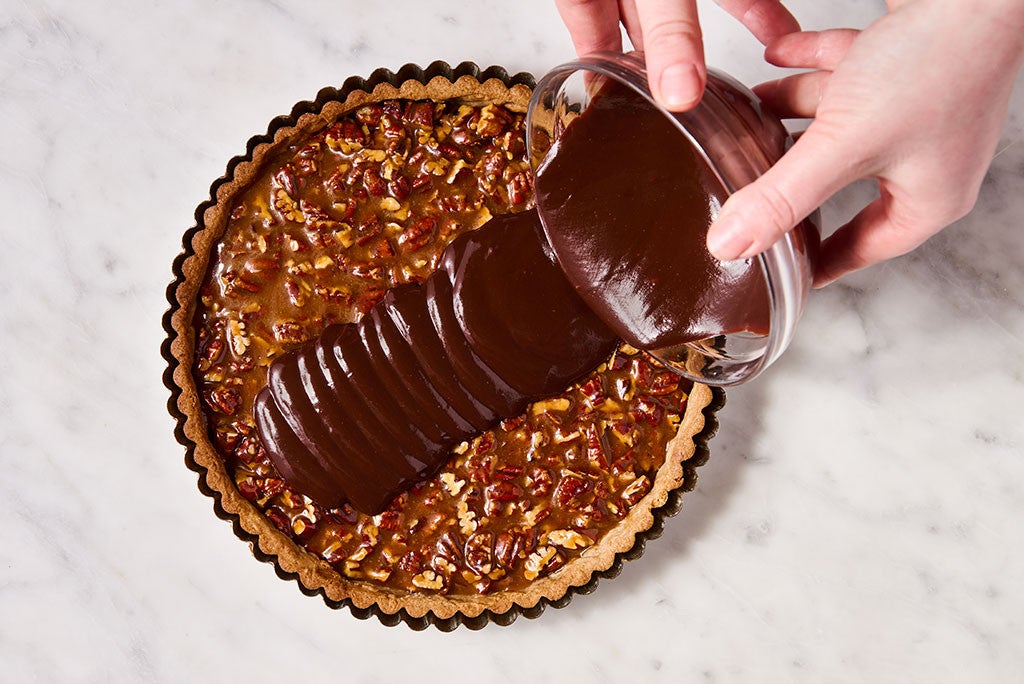 A person pouring chocolate onto pecan caramel