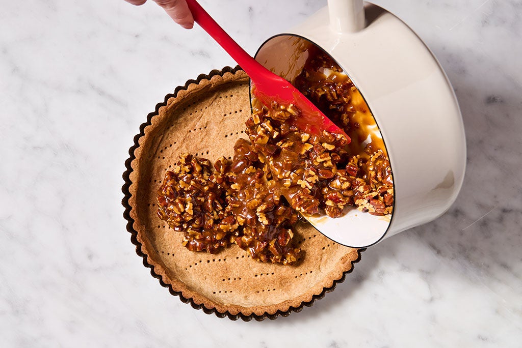 A person using a spatula to spoon caramel filling into a tart crust