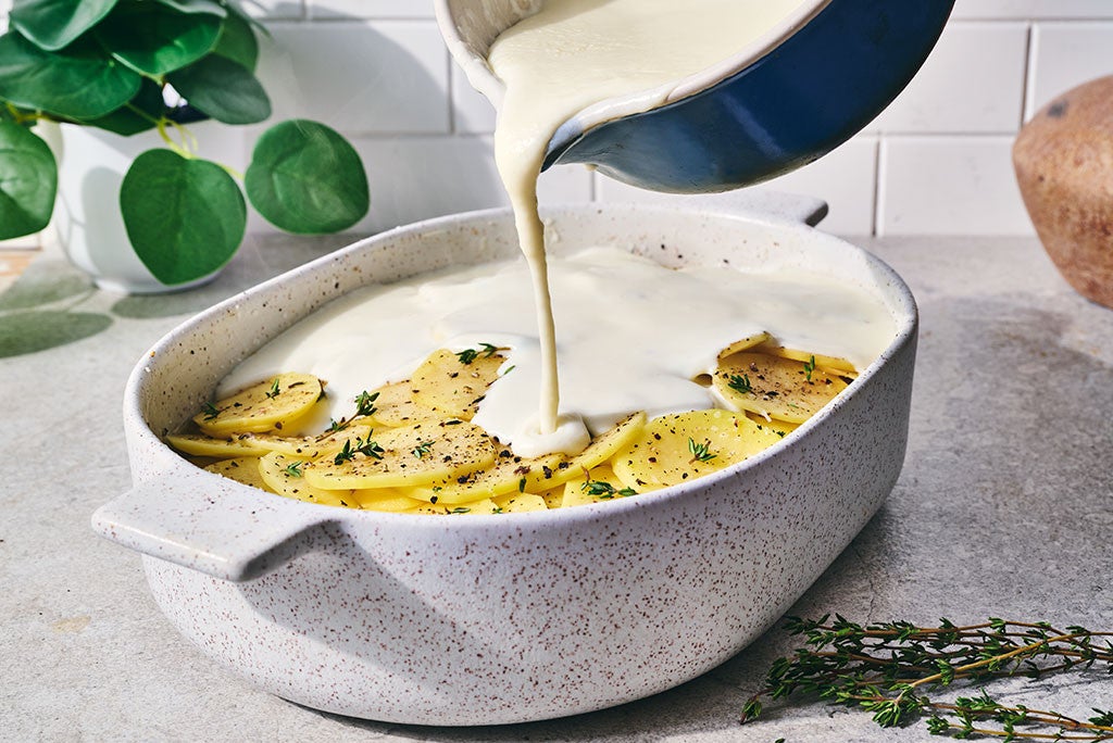 Pouring sauce over scalloped potatoes before baking them