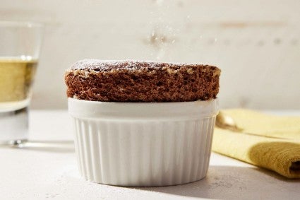 A side angle of a chocolate souffle perfectly risen in a ramekin.