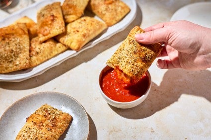 A Homemade Pizza Pocket being dipped in marinara sauce