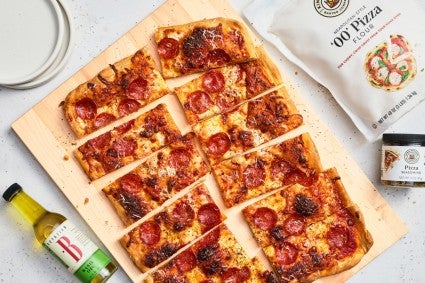 Sliced sheet pan pizza next to flour bag, pizza seasoning, and pizza oil