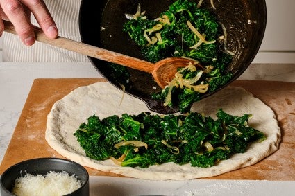 Sauteed greens being placed on pizza dough 