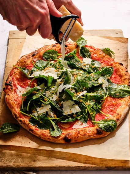 Salad pizza being dressed with shaved cheese