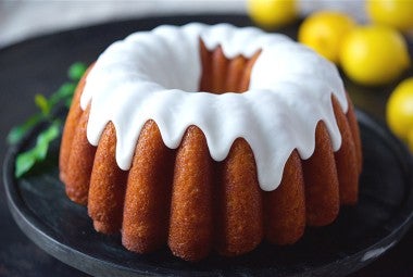 A side angle photo of Glazed Lemon Bundt Cake. The cake has a thick white glaze on top that is delicately dripping down the sides of the cake.